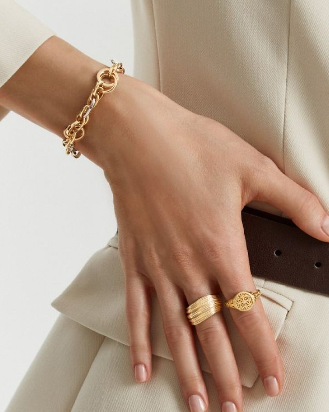 Mão com pulseira de elos e anéis folheados a ouro
